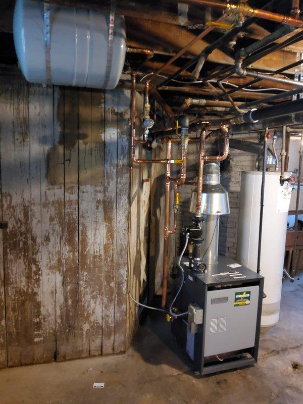 Completed installation of Weil McLain CGA-6 hot water boiler system in basement mechanical room. Installation included mounting and connecting new boiler unit, expansion tank, pressure reducing valve, backflow preventer, automatic air vent, and circulator pump with all necessary near boiler piping modifications using copper pipe. Installed new flue pipe venting to existing chimney, ran dedicated electrical circuit for boiler operation, and mounted new digital programmable thermostat for system control. All components tested and verified operational upon completion.