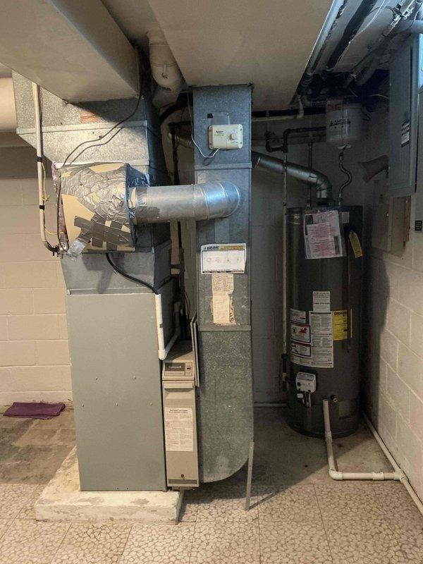 Conducted furnace replacement estimate for 26-year-old American Standard unit located in basement utility room. Documented existing equipment configuration including furnace, ductwork connections, and surrounding mechanical systems with photographs for proposal preparation.
