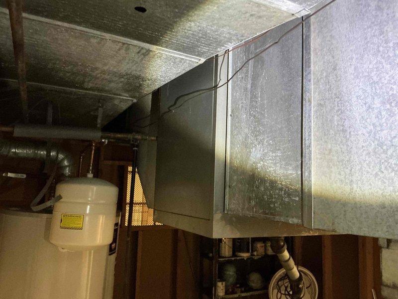 Removed non-functioning air cleaner unit from existing HVAC system and installed replacement ductwork to restore proper airflow. Modified sheet metal ductwork connections to integrate with existing copper piping and mechanical components in utility space, ensuring proper clearances around expansion tank and heating system elements.