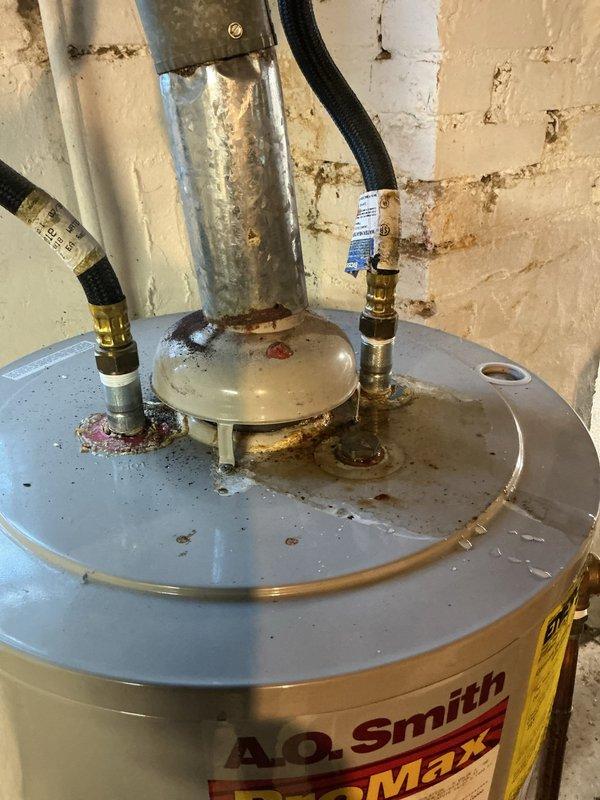 Responded to service call for tanked water heater leaking from top connections following recent tank flush. Upon inspection, found A.O. Smith ProMax water heater with significant corrosion and rust buildup at top fitting connections and center access panel, indicating long-term moisture exposure that likely worsened after flushing procedure disturbed sediment and stressed compromised fittings.