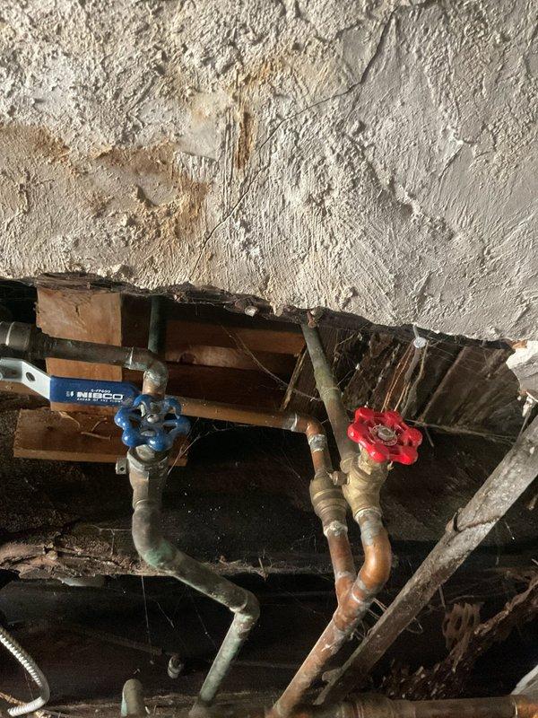 Responded to emergency plumbing call for active water leak penetrating through second floor ceiling with visible bulging. Upon investigation, identified compromised piping in crawlspace above affected area, evidenced by water staining on ceiling surface and aged copper supply lines showing deterioration. Accessed plumbing assembly beneath floor joists, inspected NIBCO valve connections, shutoff valves, and associated copper and PVC piping for failure points. Isolated water supply using existing red-handle shutoff valve to stop active leak. Assessed bathroom fixtures including tub spout and shower valve for related issues, noting mineral buildup and age-related wear on chrome fixtures. Documented existing conditions of plumbing system, structural water damage to ceiling material, and compromised pipe sections requiring repair or replacement to prevent further water intrusion.