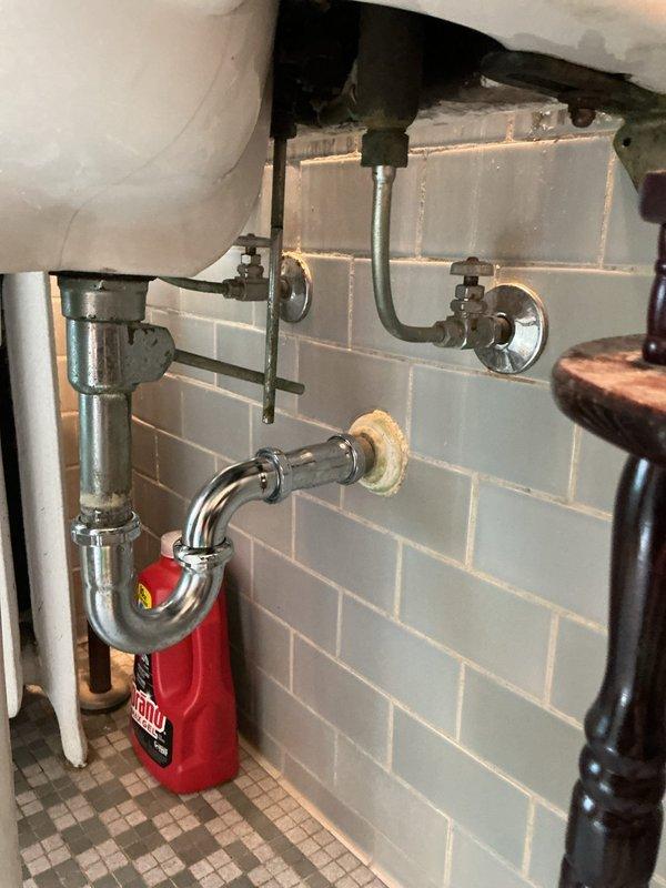 Responded to service call for leaky faucet repair and plumbing inspection. Upon arrival, inspected under-sink plumbing installation including chrome P-trap drain assembly, shut-off valves, and supply line connections. Examined Kohler shower valve fixture with cross-style handle for potential leaks and proper operation. Identified moisture presence on shower valve and surrounding wall surface. Verified all plumbing connections, checked for loose fittings at threaded connections and wall penetration points, and assessed condition of existing sealant. Completed visual inspection of accessible plumbing components and documented findings with photographic evidence for service records.