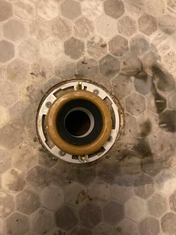 Responded to a water leak at the laundry drain pipe during normal business hours. Upon inspection, identified significant corrosion and rust buildup on the drain fixture assembly, with evidence of long-term moisture exposure and mineral deposits causing deterioration of the drain components. Documented the condition of the hexagonal tile floor surrounding the drain, noting water staining, grime accumulation in grout lines, and visible wear patterns consistent with chronic water leakage. The drain fixture showed advanced oxidation on metal components with rust-colored staining extending to surrounding floor surfaces. Photographed the affected areas for service records, capturing the extent of corrosion on the concentric ring assembly and the deteriorated condition of the floor tiles adjacent to the leak source.