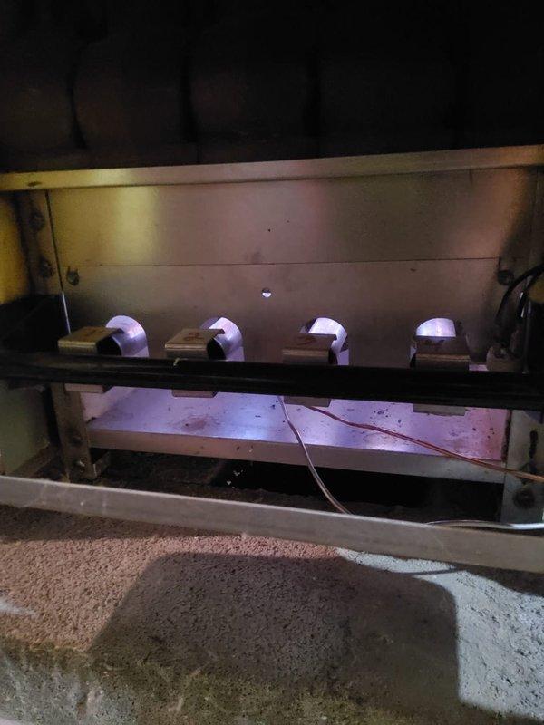 Completed maintenance inspection on 20-year-old steam boiler system located in basement. Performed visual assessment of burner assembly, heat exchanger sections, and gas supply components. Inspected burner tubes showing purple flame indication, examined cast iron heat exchanger sections displaying moderate dust and sediment accumulation on outer sections with center section appearing cleaner. Noted age-appropriate surface discoloration and minor deposits on heat exchanger fins consistent with two decades of operation. System operational at time of inspection with burner assembly functioning properly.