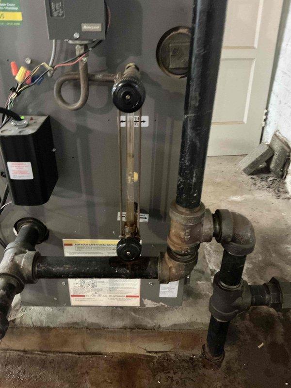 Conducted on-site estimate for replacement of 20-year-old Lennox boiler system showing significant deterioration. Assessed existing equipment condition, noting extensive rust and corrosion on aged metal piping, deteriorated concrete pad foundation, and overall system wear consistent with end-of-service-life status. Documented equipment configuration including sight glass assembly, copper supply lines, venting system, electrical connections, and associated plumbing infrastructure for replacement specifications and proposal preparation.