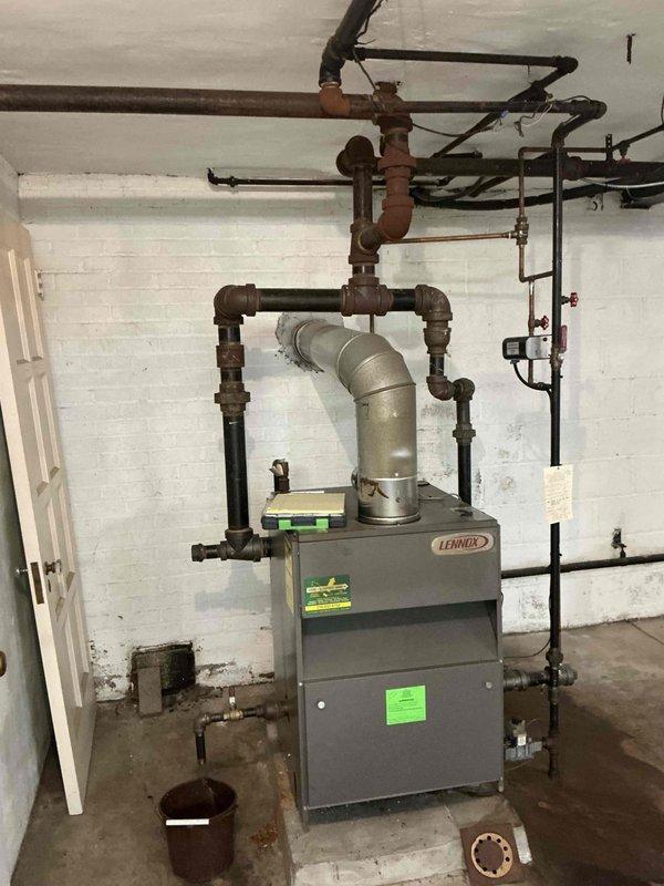 Conducted on-site estimate for replacement of 20-year-old Lennox boiler system showing significant deterioration. Assessed existing equipment condition, noting extensive rust and corrosion on aged metal piping, deteriorated concrete pad foundation, and overall system wear consistent with end-of-service-life status. Documented equipment configuration including sight glass assembly, copper supply lines, venting system, electrical connections, and associated plumbing infrastructure for replacement specifications and proposal preparation.