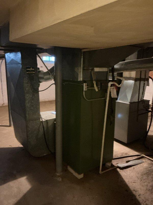Conducted comprehensive on-site evaluation of existing residential HVAC system located in basement utility area for furnace replacement estimate. Documented current equipment configuration including existing beige/tan furnace unit with associated ductwork connections, green system components, and water heater placement. Assessed mechanical room layout, ceiling joist clearances, existing duct routing, and available space for new equipment installation. Photographed equipment specifications, warning labels, utility connections, and surrounding infrastructure to prepare detailed replacement proposal for homeowner consideration.