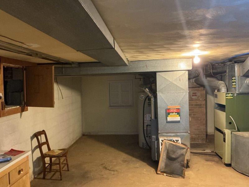 Conducted comprehensive on-site evaluation of existing residential HVAC system located in basement utility area for furnace replacement estimate. Documented current equipment configuration including existing beige/tan furnace unit with associated ductwork connections, green system components, and water heater placement. Assessed mechanical room layout, ceiling joist clearances, existing duct routing, and available space for new equipment installation. Photographed equipment specifications, warning labels, utility connections, and surrounding infrastructure to prepare detailed replacement proposal for homeowner consideration.