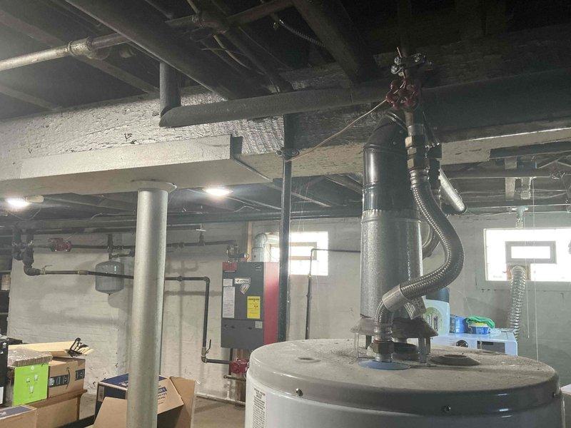 Completed on-site evaluation and documentation of existing boiler heating system in residential basement mechanical room. Assessed current hydronic heating unit with red and black exterior panel, including evaluation of associated piping network, circulation pump, and connections to overhead distribution system. Photographed existing water heater, ductwork, and overall mechanical room layout to provide comprehensive estimate documentation for potential boiler replacement or upgrade.