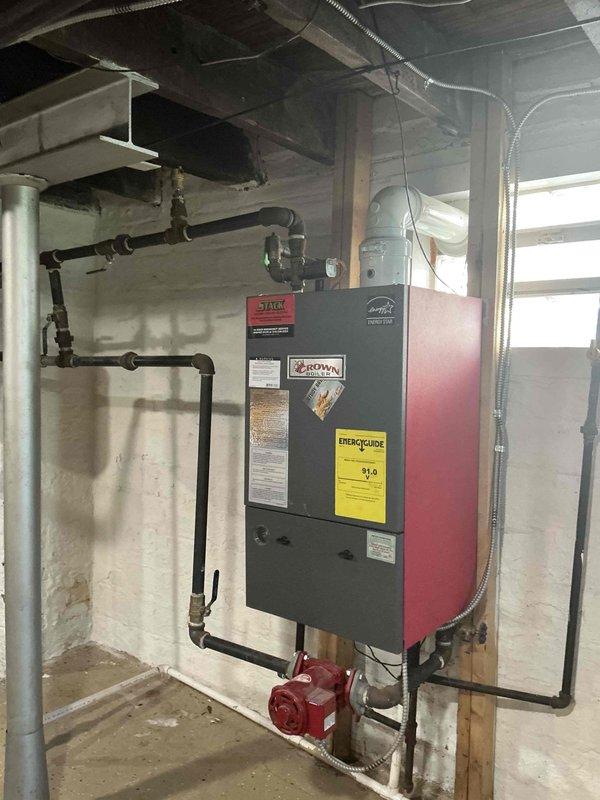 Completed on-site evaluation and documentation of existing boiler heating system in residential basement mechanical room. Assessed current hydronic heating unit with red and black exterior panel, including evaluation of associated piping network, circulation pump, and connections to overhead distribution system. Photographed existing water heater, ductwork, and overall mechanical room layout to provide comprehensive estimate documentation for potential boiler replacement or upgrade.