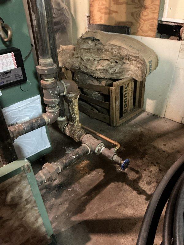Performed scheduled maintenance on a 2-year-old steam boiler system. Upon inspection, discovered significant water damage throughout the mechanical room, including heavily stained concrete flooring and deteriorated materials indicating ongoing moisture infiltration issues. Examined copper piping system showing age-related corrosion with visible green patina on surfaces, along with associated valves and fittings. Assessed damaged insulation material in overhead areas with torn sections and deterioration requiring attention. Documented conditions of HVAC equipment and surrounding infrastructure affected by prolonged water exposure. Recommended addressing moisture source and water intrusion problems to prevent further deterioration of mechanical systems and building components.