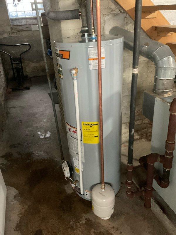 Completed warranty replacement of residential water heater in basement utility area. Removed existing failed unit and installed new white cylindrical water heater with proper connections including copper supply lines, expansion tank at base, and venting system. Configured control assembly with temperature settings and verified all plumbing connections, gas line hookup via flexible corrugated tubing, and proper clearances around unit. Service was scheduled after completion of separate boiler preventive maintenance to avoid conflicts between technicians working in same space.