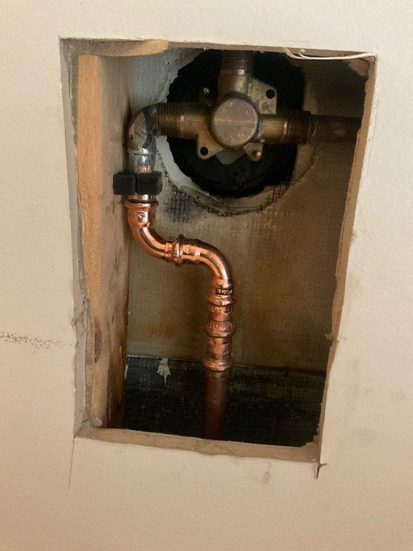Responded to active water leak originating from shower valve assembly with visible water damage to dining room ceiling below. Upon inspection, identified significant moisture intrusion evidenced by brown discoloration and staining pattern on ceiling surface. Created access opening in wall to expose shower mixing valve and supply lines. Discovered failed connection at shower valve causing water to leak through wall cavity and penetrate dining room ceiling. Repaired compromised plumbing connection and addressed copper supply line configuration to restore proper water flow and eliminate leak source.