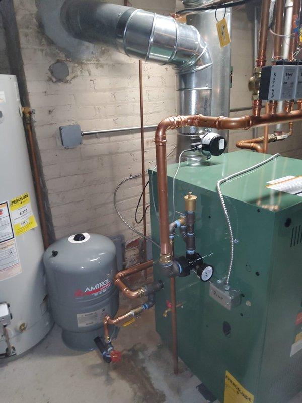 Completed full boiler replacement in residential basement, installing New Yorker model CG70 cast iron hot water boiler rated at 210,000 BTUs. Installation included new Amtrol expansion tank, pressure reducing valve with backflow preventer, automatic air vent, and circulator pump. Performed all near boiler piping modifications using copper pipe and brass fittings, and installed new flue pipe connection to existing chimney. Reused existing thermostats, zone valves, and zone panel from previous system. System tested and operational with limited lifetime warranty on heat exchanger, 5-year parts, and 5-year labor coverage.