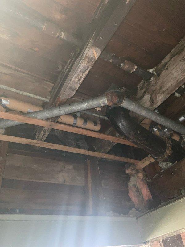 Responded to emergency plumbing call for multiple leaking pipes with exposed access through open ceiling soffit. Replaced deteriorated galvanized steel supply line and galvanized sink sanitary line that were actively leaking. Additionally addressed steam heating system issues by performing boiler skimming procedure on VEH boiler and repaired leaking steam supply pipe at joint connection. All repairs completed with accessible piping in exposed structural areas as documented in photos showing aged wooden joists and existing plumbing infrastructure.