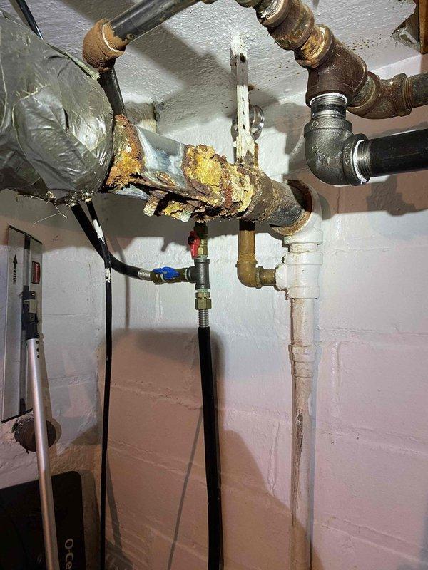 Responded to service call for 3-year-old steam boiler system with reported pipe corrosion. Upon inspection, identified severe corrosion on horizontal steam pipe with extensive rust buildup, pitting, and metal deterioration requiring immediate repair. Documented existing plumbing configuration including copper risers, brass fittings, and connection points to facilitate proper repair planning and parts procurement.