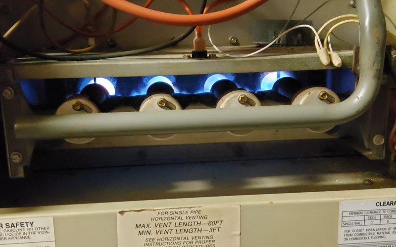 Responded to service call for 10-year-old furnace reported not heating properly. Performed comprehensive clean and check maintenance service on gas furnace system. Inspected combustion chamber and confirmed all four burners igniting properly with clean blue flames. Verified gas manifold connections secure and operating within specifications. Checked blower assembly, heat exchanger, and all safety controls for proper operation. Cleaned burner assembly and combustion area. Inspected venting system and confirmed proper draft. Tested thermostat operation and system cycling. Documented equipment condition with photos showing active burner operation and overall unit condition in basement installation. Unit operational and heating effectively upon service completion.