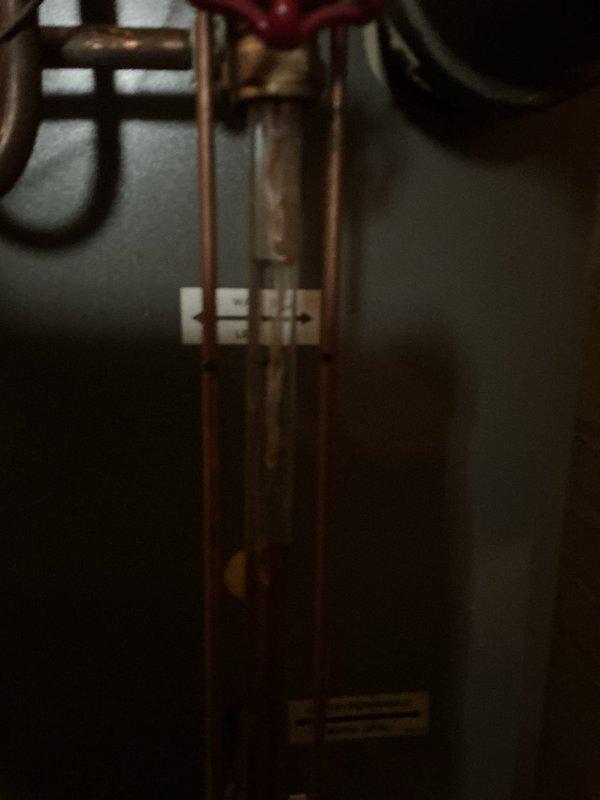Responded to service call for 15-year-old boiler in basement exhibiting loud rumbling sound followed by perking noise. Upon arrival, performed visual inspection of boiler system and associated plumbing components, documenting aged galvanized piping with visible corrosion and deteriorated fittings. Examined copper piping connections, pressure vessel, and control valves for signs of kettling, sediment buildup, or mechanical failure that could cause reported noise issues. Photographed system components including corroded horizontal pipe sections showing green patina oxidation and worn threaded unions near floor level. Assessed overall condition of 12-13 year old heating system and surrounding infrastructure showing significant age-related wear.