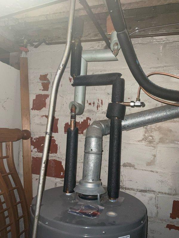 Performed an on-site evaluation for a tankless water heater conversion, inspecting the existing tank-style unit with insulated copper supply and return lines and a galvanized flue connected to a larger vent duct. Assessed basement conditions, including overhead pipe routing, available wall space, and ventilation and venting options to determine installation requirements for a tankless unit. Documented all conditions with photos to support the recommended scope of work.