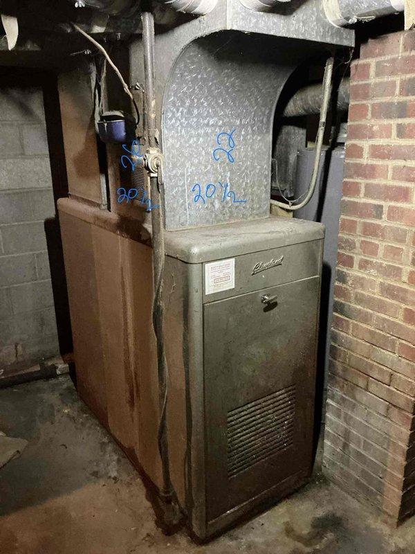 Performed an on-site estimate for replacement of an aged upright gas furnace in the basement, which showed heavy corrosion and rust staining along the cabinet's lower-left panel. Documented the existing unit and measured the supply plenum and duct transitions (approx. 20½" and 22") to confirm sizing and fit for a like-for-like replacement. Photographed the equipment, flue piping, wiring, and surrounding clearances to support the replacement scope.