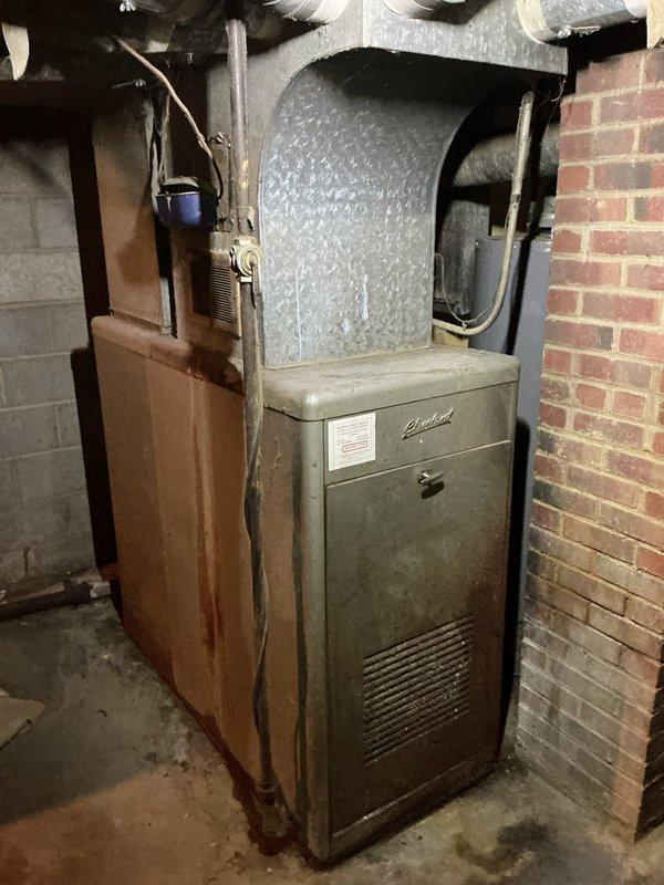 Performed an on-site estimate for replacement of an aged upright gas furnace in the basement, which showed heavy corrosion and rust staining along the cabinet's lower-left panel. Documented the existing unit and measured the supply plenum and duct transitions (approx. 20½" and 22") to confirm sizing and fit for a like-for-like replacement. Photographed the equipment, flue piping, wiring, and surrounding clearances to support the replacement scope.