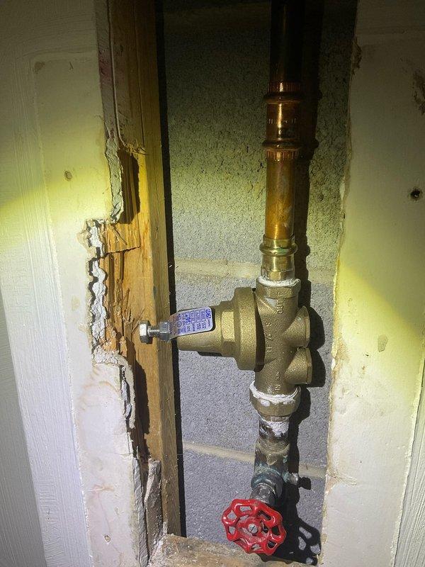 Removed and replaced the existing 50-gallon electric water heater with a new Bradford White unit, reconnecting the copper supply piping, expansion tank, and electrical supply, then tested for proper operation with no leaks. Also verified the water pressure reducing valve and shutoff valve assembly accessed through the wall opening.