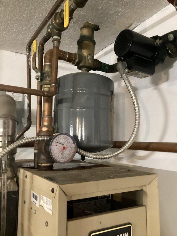 Responded to service call regarding oil leakage from heating system. Upon inspection, determined that the boiler expansion tank is leaking. Documented the plumbing installation with photos showing the failing expansion tank mounted near ceiling, copper pipe network, and associated valves and fittings. Scheduled follow-up appointment to provide estimates for both repair options and complete system replacement.