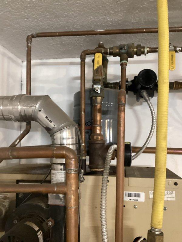 Responded to service call regarding oil leakage from heating system. Upon inspection, determined that the boiler expansion tank is leaking. Documented the plumbing installation with photos showing the failing expansion tank mounted near ceiling, copper pipe network, and associated valves and fittings. Scheduled follow-up appointment to provide estimates for both repair options and complete system replacement.