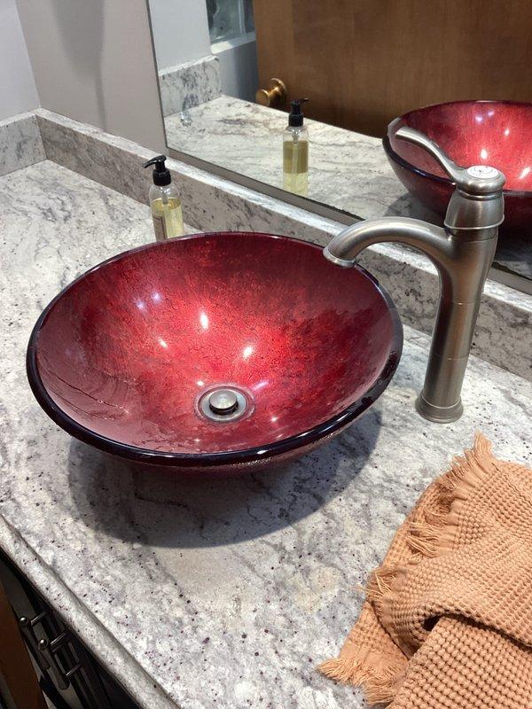 Completed installation of two customer-supplied toilets in master and hallway bathrooms, removing the existing fixtures. Additionally, removed old top mount sink in hallway bathroom and installed new customer-supplied vessel-style sink with distinctive red bowl, making all necessary water connections and ensuring proper function.