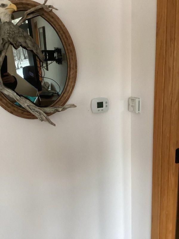 Relocated thermostat from its original position where direct sunlight was causing inaccurate temperature readings. Installed new wiring through ceiling joists in unfinished basement area and mounted the thermostat in a more suitable location away from solar exposure to ensure proper HVAC system operation and temperature control.