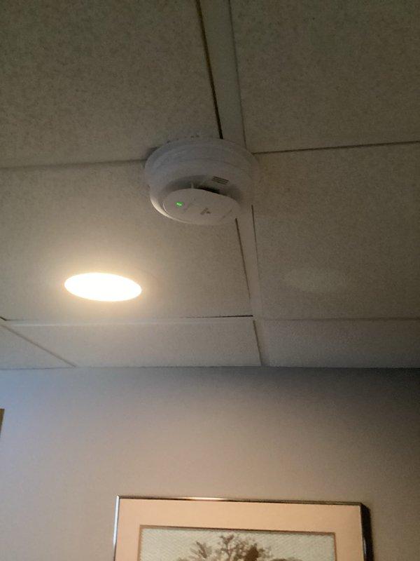 Responded to service call for smoke detector maintenance. Replaced batteries in two ceiling-mounted smoke detectors - one in a drop ceiling location and one on a textured drywall ceiling. Confirmed proper operation of both units as evidenced by illuminated green indicator lights.