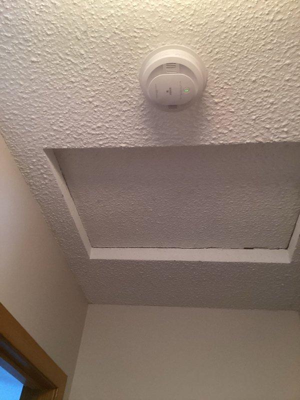 Responded to service call for smoke detector maintenance. Replaced batteries in two ceiling-mounted smoke detectors - one in a drop ceiling location and one on a textured drywall ceiling. Confirmed proper operation of both units as evidenced by illuminated green indicator lights.
