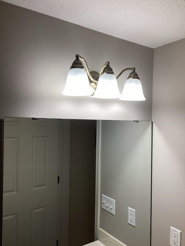 Completed installation of new outdoor receptacle on existing garage switch circuit. Replaced two bathroom vanity light fixtures, each with three bell-shaped frosted glass shades and brushed nickel finish. Installed new exterior light fixture per approved bid specifications.