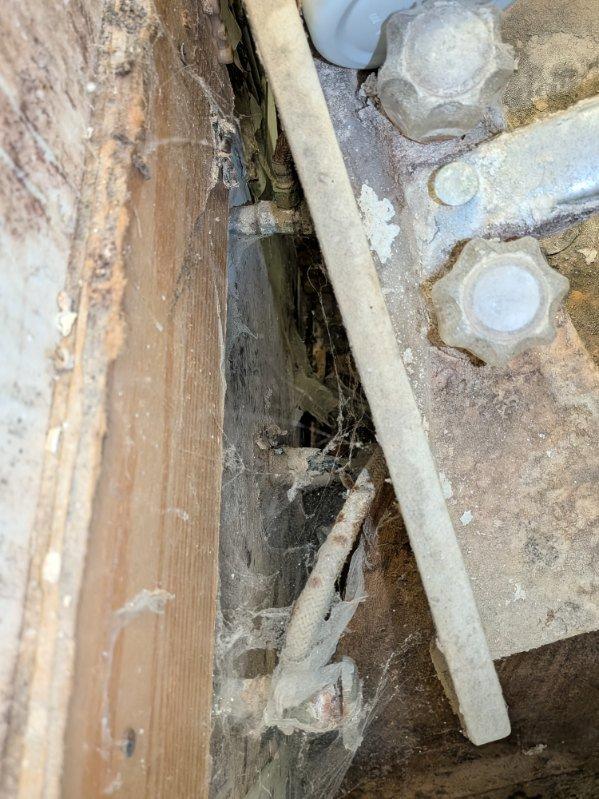 Performed diagnostic inspection of bathroom sink requiring repairs. Accessed and examined plumbing infrastructure behind wall, noting significant dust accumulation and aging components. Provided assessment for replacing existing fixtures with new 24" vanity, faucet, and complete drainage assembly.