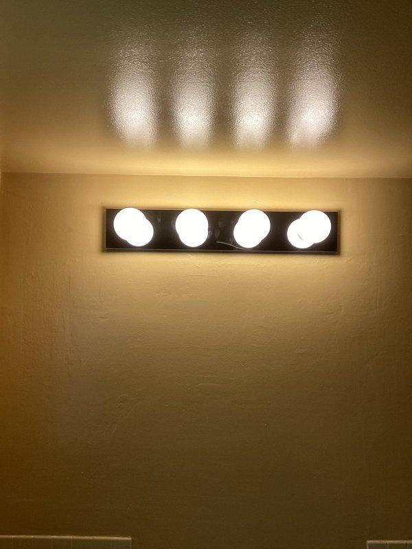 Installed customer-provided vanity light fixture in bathroom, replacing existing unit. Successfully restored illumination to basement bathroom. Verified proper operation of new fixture with all four bulbs functioning correctly and mounted securely to wall.