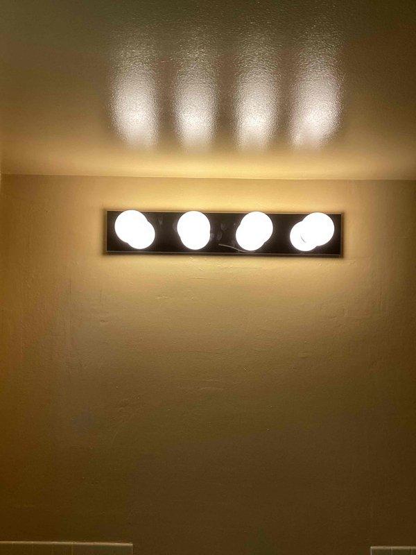 Installed customer-provided vanity light fixture in bathroom, replacing existing unit. Successfully restored illumination to basement bathroom. Verified proper operation of new fixture with all four bulbs functioning correctly and mounted securely to wall.