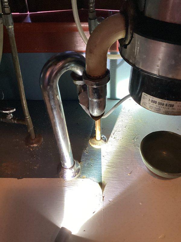 Responded to customer report of kitchen drain leak. Inspection revealed stainless steel goose neck drain under garbage disposal had developed a hole causing the leak. Removed damaged drain assembly and installed new 1 1/2" PVC drain assembly, resolving the issue.