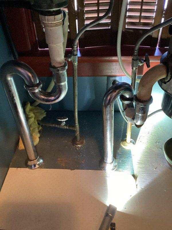 Responded to customer report of kitchen drain leak. Inspection revealed stainless steel goose neck drain under garbage disposal had developed a hole causing the leak. Removed damaged drain assembly and installed new 1 1/2" PVC drain assembly, resolving the issue.