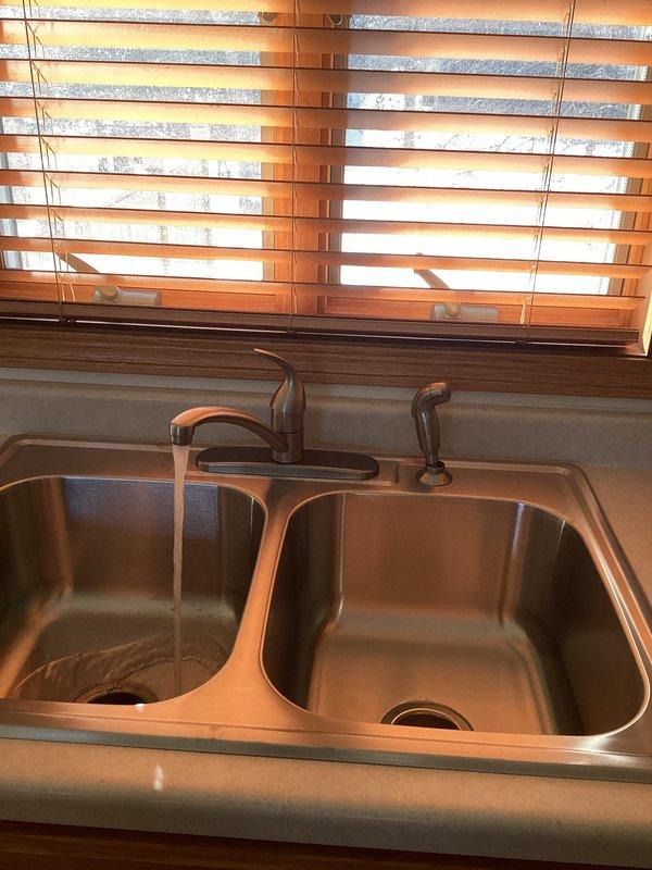 Successfully installed new kitchen faucet with side sprayer and reconnected existing garbage disposal. Verified proper water flow and drainage through the double basin sink, confirming no leaks at connection points throughout the P-trap configuration and disposal unit.