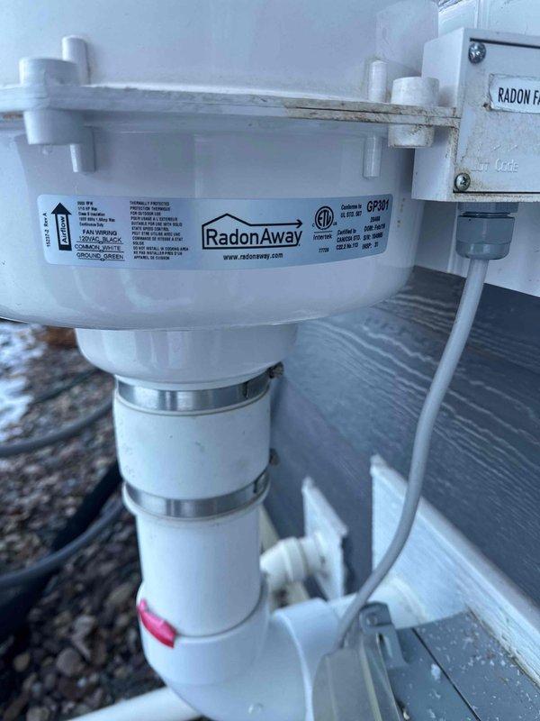 Responded to customer call regarding noise from mechanical room. Diagnosed failed radon mitigation fan due to ice buildup. System includes a RadonAway GP501 fan unit mounted to exterior wall with PVC piping connections. Provided customer with replacement fan estimate.