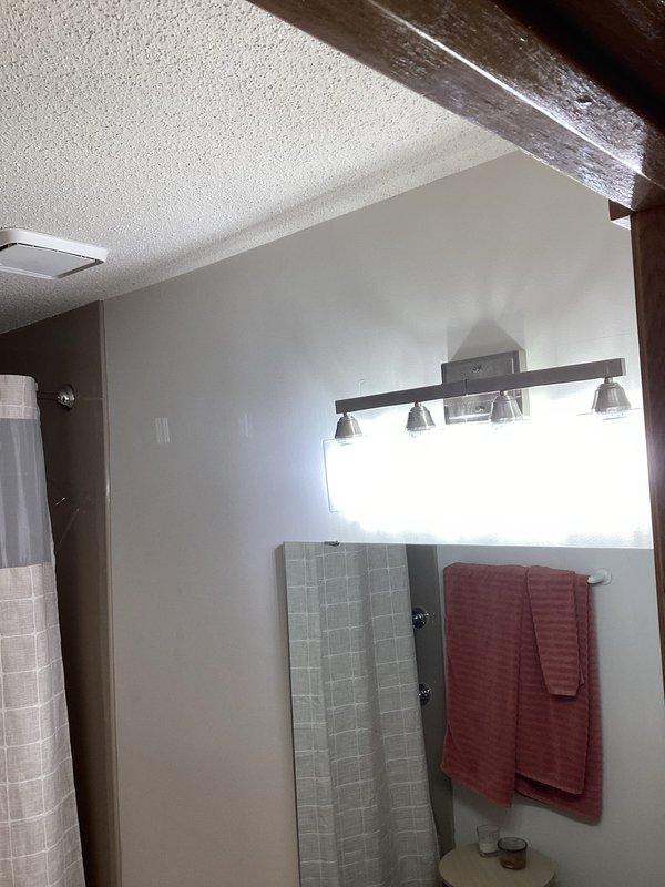 Installed customer-provided vanity light fixture in bathroom above mirror, ensuring proper wiring connections and secure mounting. Fixture features three spotlights on horizontal metal bar and is functioning correctly.