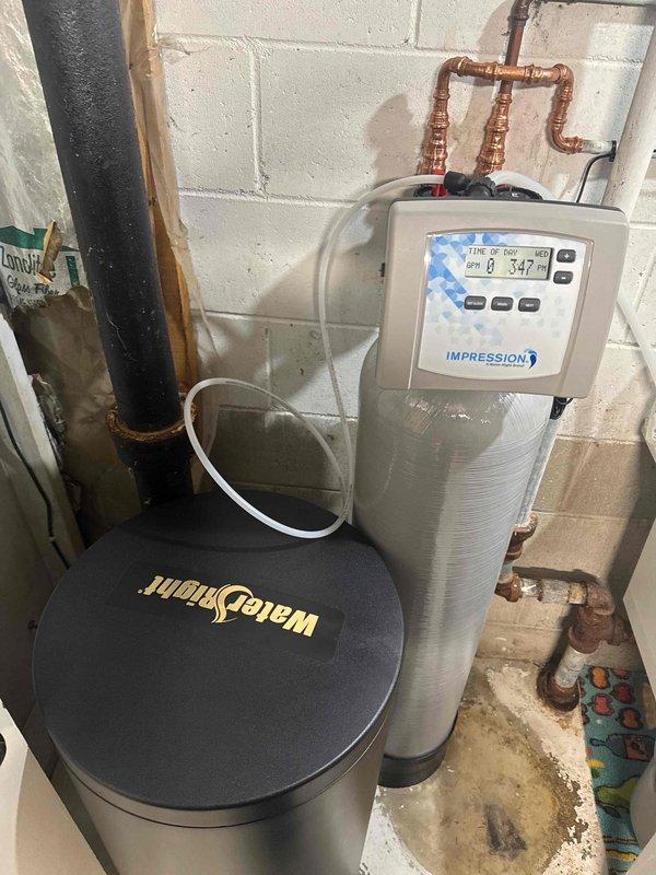 Installed new WaterRight water softening system with Impression control panel in customer's utility area. System includes a black cylindrical water softener tank and taller gray filtration tank, both connected to existing copper plumbing. Also drained water heater as part of the service.