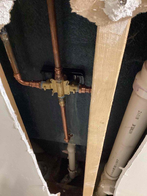 Installed customer-provided shower valve after removing old hardware, requiring access to the wall cavity to make proper copper pipe connections. Successfully completed installation of dual showerhead system with both fixed and handheld components, testing functionality to confirm proper water flow through both the tub spout and shower heads.