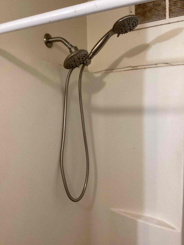 Installed customer-provided shower valve after removing old hardware, requiring access to the wall cavity to make proper copper pipe connections. Successfully completed installation of dual showerhead system with both fixed and handheld components, testing functionality to confirm proper water flow through both the tub spout and shower heads.