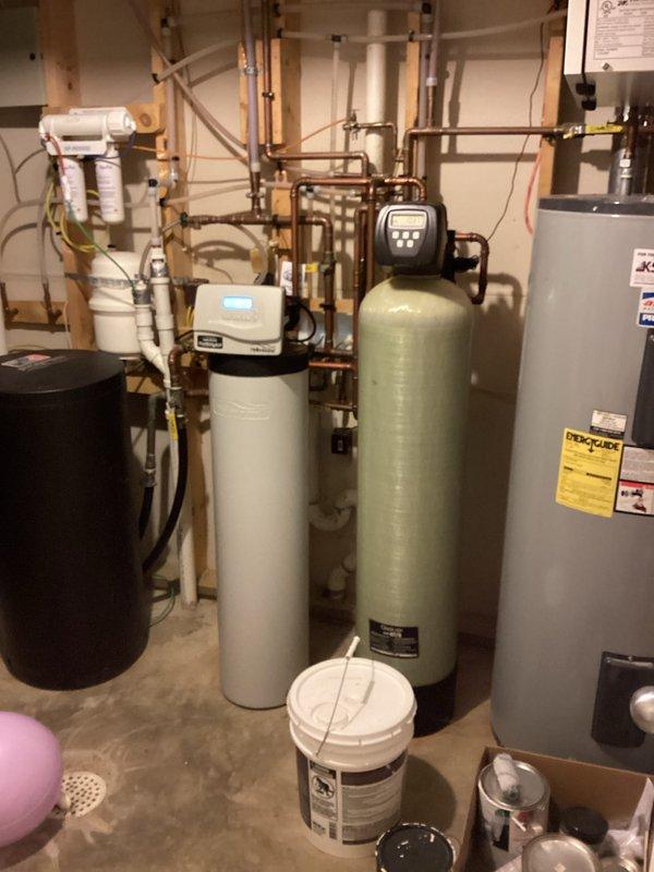 Conducted a comprehensive plumbing inspection of residential property with arrival between 8-12. Examined water treatment system (water softener, filtration tank), water heater, and associated plumbing connections throughout utility room. All systems were found to be in excellent working condition with no issues requiring repair or maintenance.