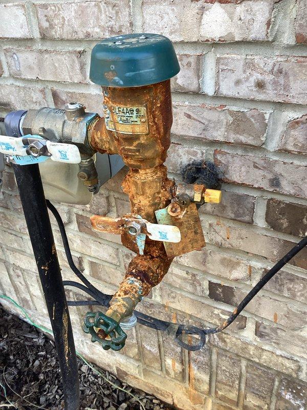 Inspected severely corroded backflow preventer for irrigation system mounted on exterior brick wall. Documented extensive rust damage and deterioration on copper pipe assembly with green valve handle. Provided customer with parts estimate for backflow preventer replacement; parts on order with expected availability within 10 days.