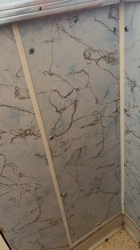 Arrived for scheduled service to address a small leak behind tub that was leaking into basement. Upon arrival, customer was not present and could not be reached by phone. Visual inspection of shower enclosure revealed likely source of leak at corner junction of decorative panels, with evidence of water damage visible in basement at P-trap connection showing mineral deposits and possible deterioration.