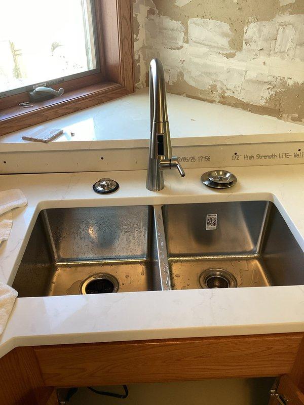 Reinstalled customer-supplied kitchen faucet and garbage disposal in double-basin stainless steel sink. Made all necessary plumbing connections including PVC drain assembly and P-trap installation. Tested both fixtures for proper operation with successful results.