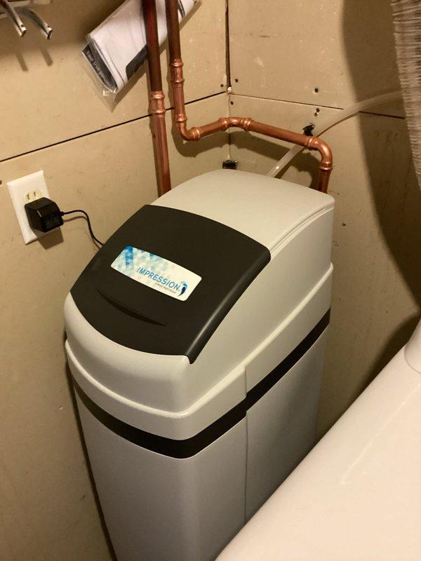 Completed installation of customer-supplied toilet and new water softener system in basement utility area. Repaired water leak at main meter with new copper piping connections and fittings. All plumbing connections were properly secured with brass valves and metal brackets to ensure system integrity. Water softener unit was installed with appropriate inlet and outlet piping, electrical connection established, and system tested for proper operation. Leak repair at main meter required replacement of deteriorated sections and installation of new shut-off valves for future maintenance access.