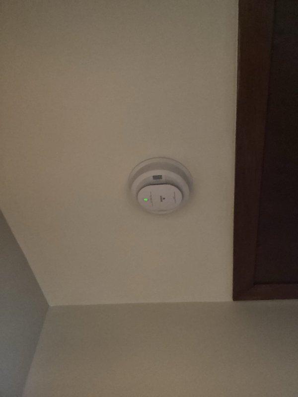 Installed combination smoke and carbon monoxide detector in hallway per approved bid. Ran 14-3 wiring from existing bedroom smoke detector to new hallway unit to ensure proper interconnection between devices. Both detectors tested and verified operational with LED indicators functioning correctly.